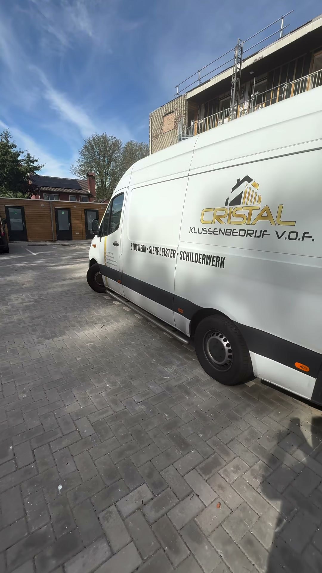 De witte bus van Cristal Klussenbedrijf met het gouden logo, geparkeerd bij een appartementengebouw in aanbouw
